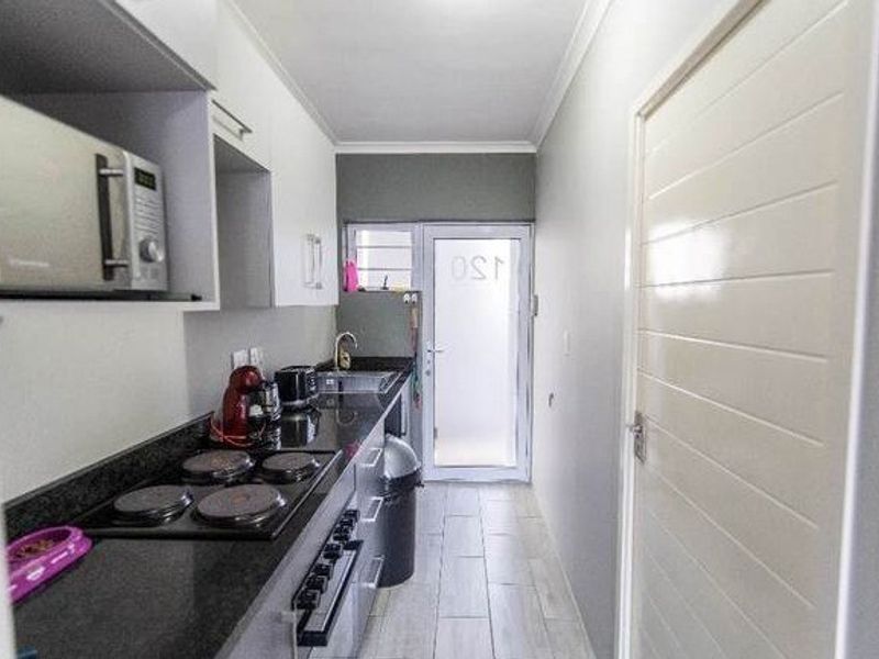 Compact galley-style kitchen featuring modern cabinetry, granite countertops, integrated electric hob and oven, and direct access to an exterior door.