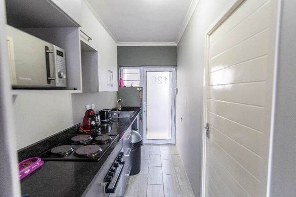 Compact galley-style kitchen featuring modern cabinetry, granite countertops, integrated electric hob and oven, and direct access to an exterior door.