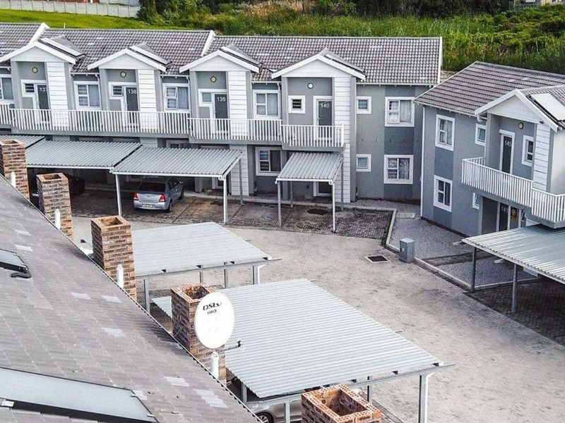 Aerial view of a modern apartment complex featuring multiple units with private carports, balconies, and paved driveway access.
