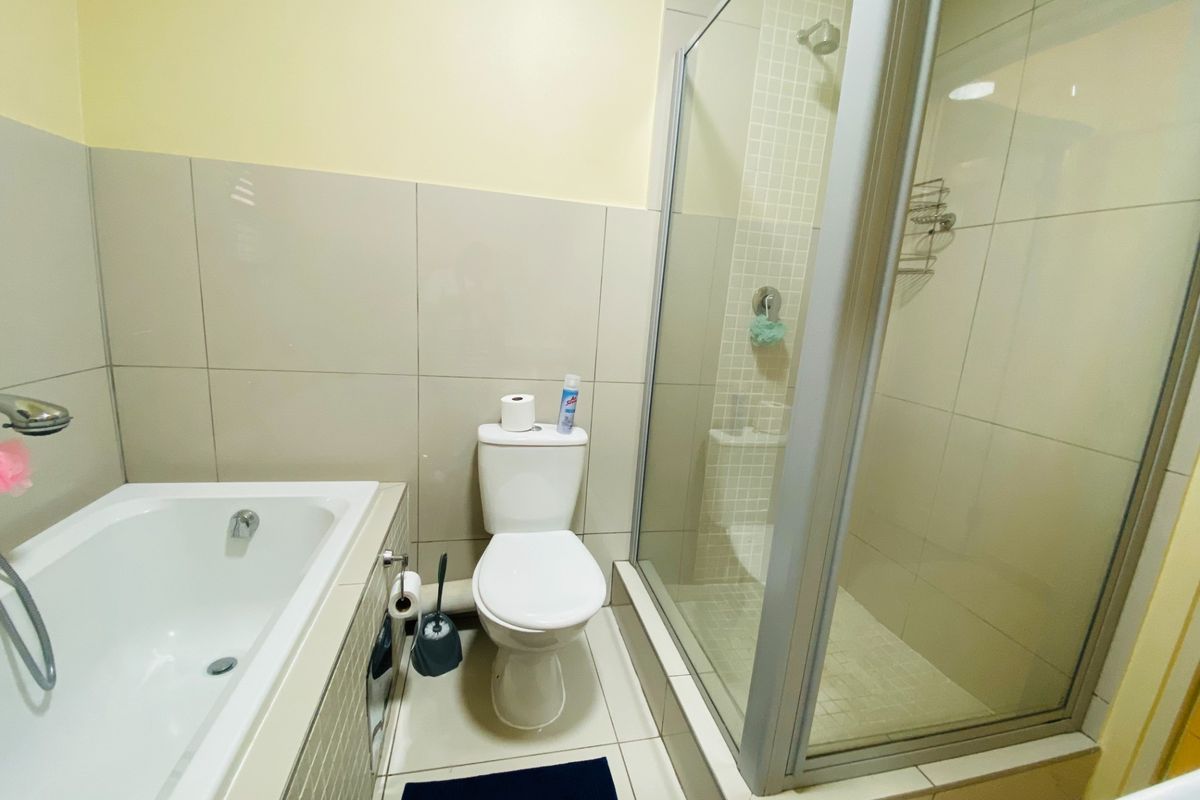 A functional bathroom featuring a built-in bathtub, a separate glass-enclosed shower, and a toilet with neutral wall and floor tiling.