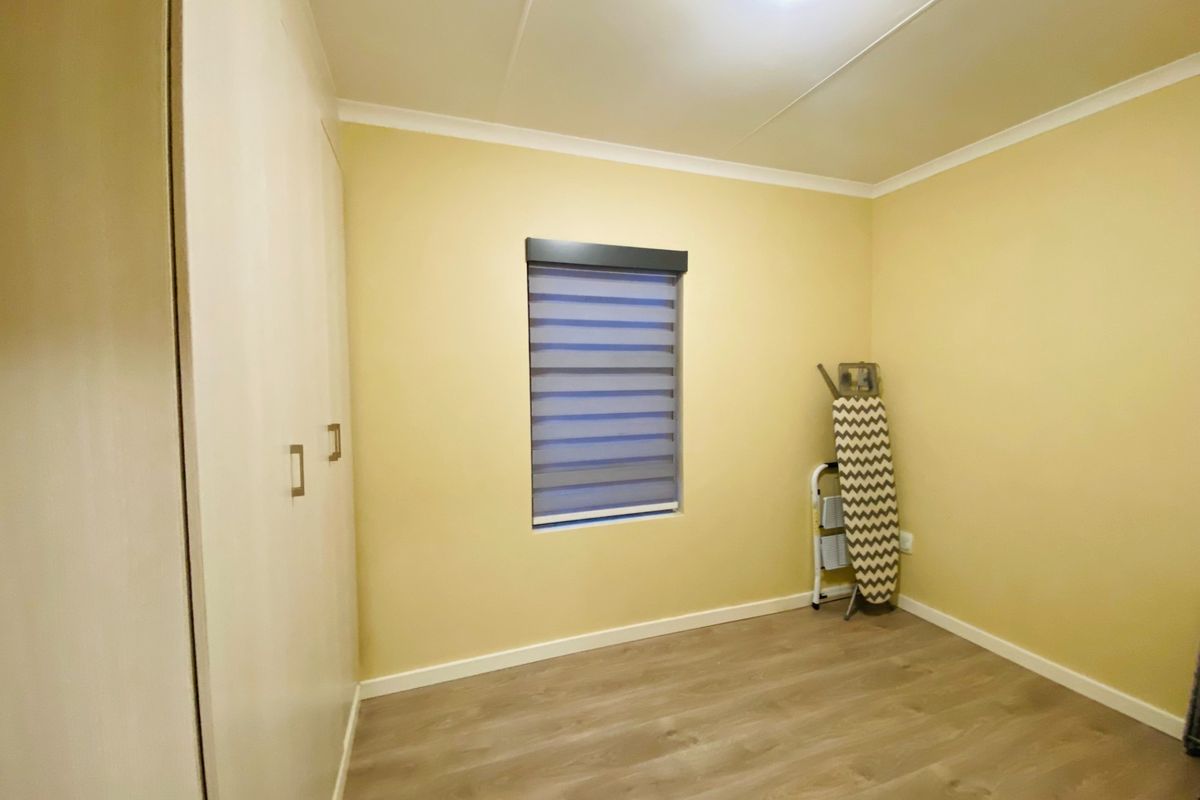 A clean, neutral bedroom featuring light laminate flooring, built-in cupboards, and a modern roller blind, offering a versatile space ready for personalization.