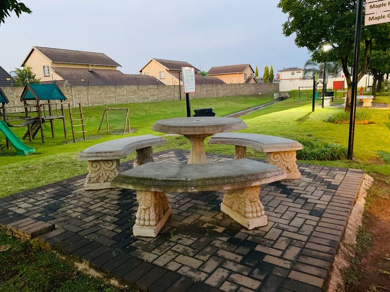 A communal garden area featuring a paved seating area with stone benches and a table, surrounded by lawn and playground equipment.