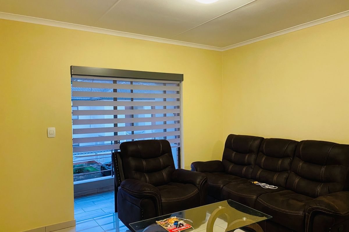 A living room featuring tiled flooring, neutral yellow walls, and modern zebra blinds, providing a bright and functional space.