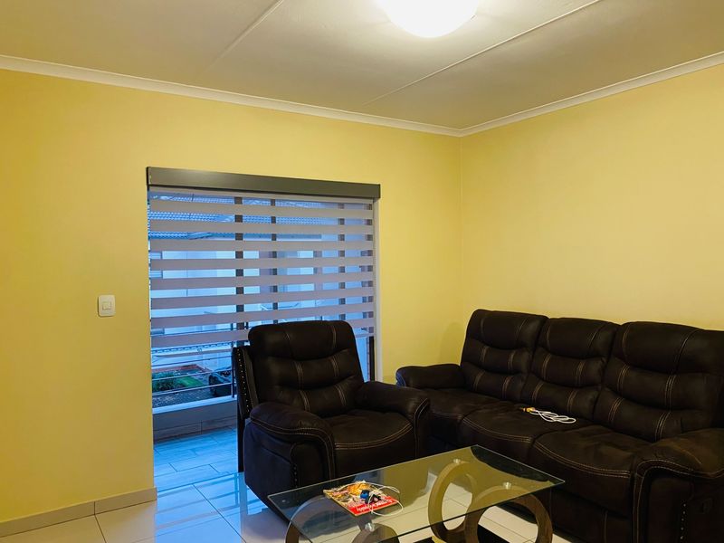 A living room featuring tiled flooring, neutral yellow walls, and modern zebra blinds, providing a bright and functional space.