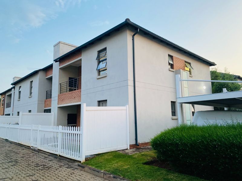 Exterior view of a modern townhouse complex featuring a paved driveway, white picket fencing, and a covered carport area.