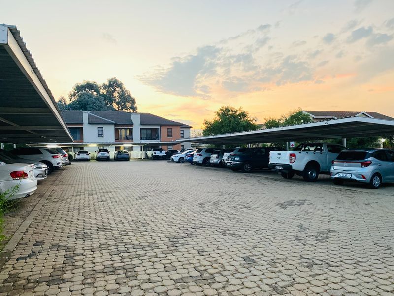 A view of the townhouse complex parking area featuring paved driveway and covered carport structures for residents.