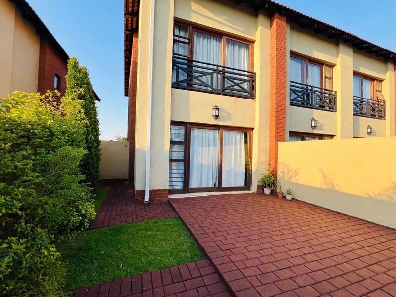 Rear view of a townhouse featuring a brick paved patio, a small garden area, and upper-level balconies with metal railings.