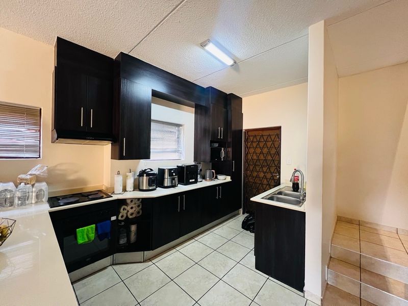 A functional kitchen featuring dark wood cabinetry, built-in oven, electric hob, and tiled flooring, providing a practical workspace with direct access to a security gate.