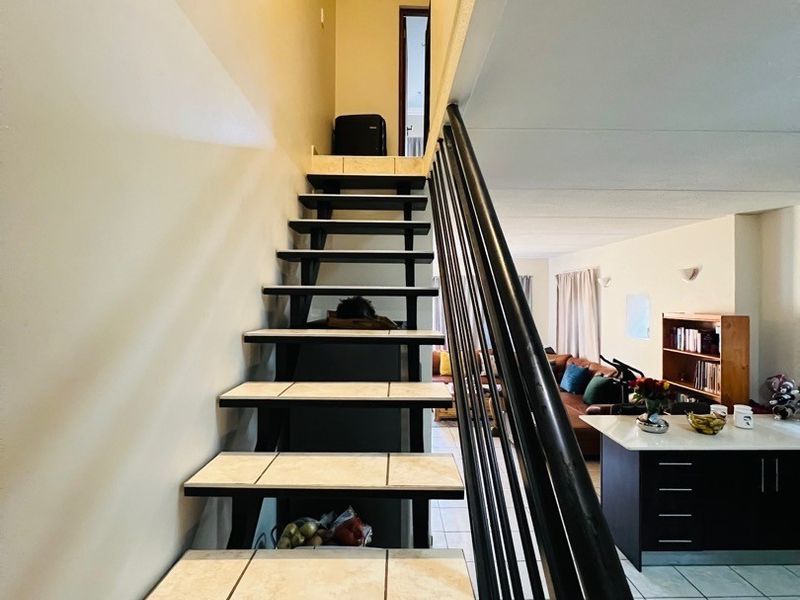 A staircase featuring tiled steps and a black metal balustrade, leading to an upper level within an open-plan living area.