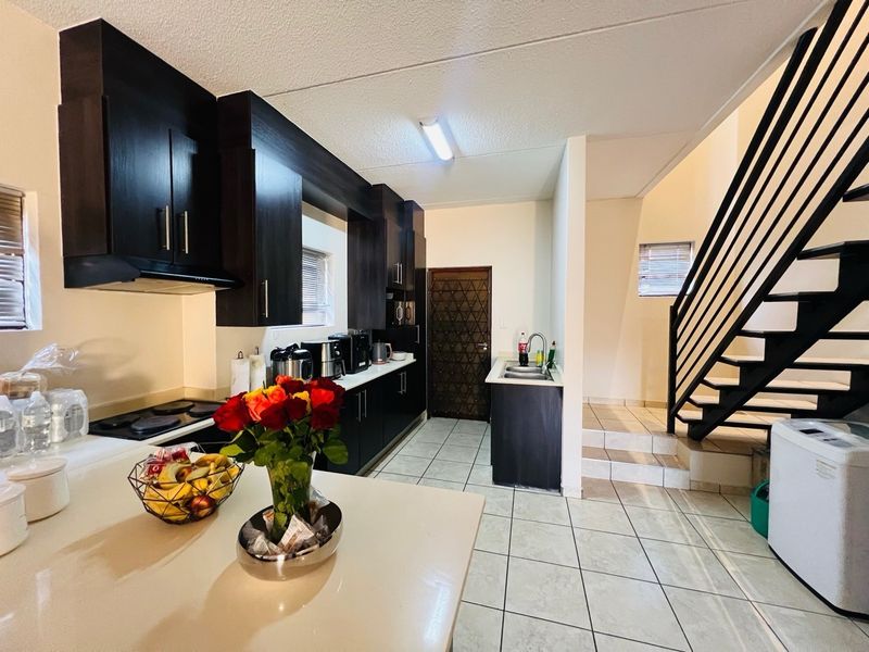A functional kitchen featuring dark cabinetry, built-in hob, extractor fan, and double sink, with an adjacent staircase leading to the upper level.