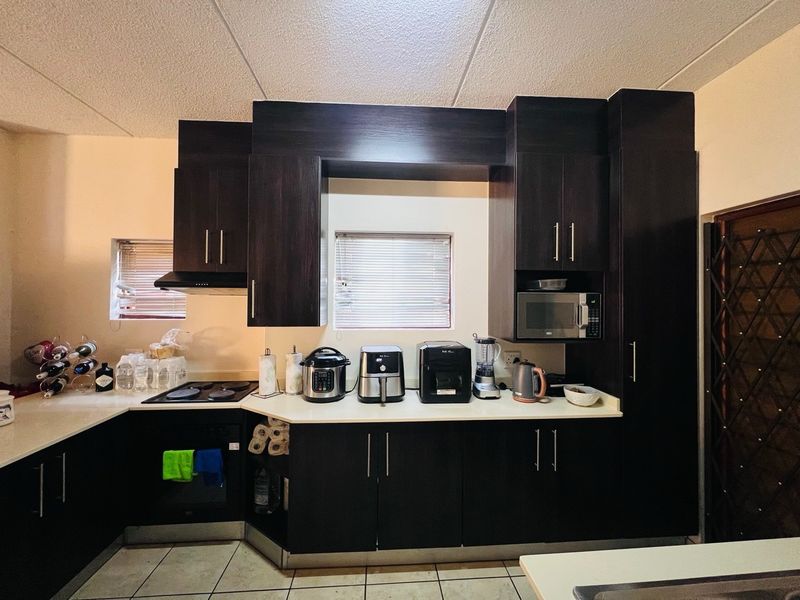 A functional kitchen featuring dark wood cabinetry, built-in oven, electric hob, and integrated microwave, complemented by tiled flooring and natural light from windows.