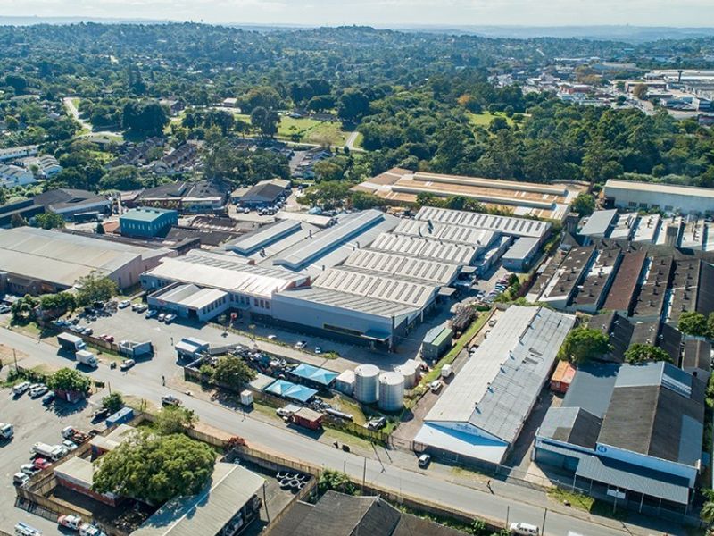 Aerial view of a large commercial industrial warehouse complex featuring multiple metal-roofed buildings, paved parking areas, and storage facilities within an urban setting.