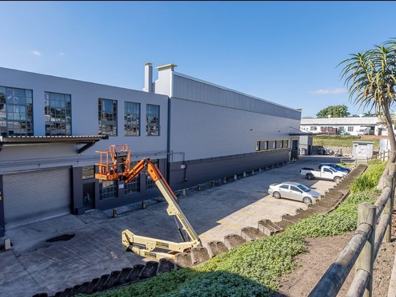 Rear exterior view of a commercial industrial building featuring a concrete yard, roller shutter access, and modern metal cladding.