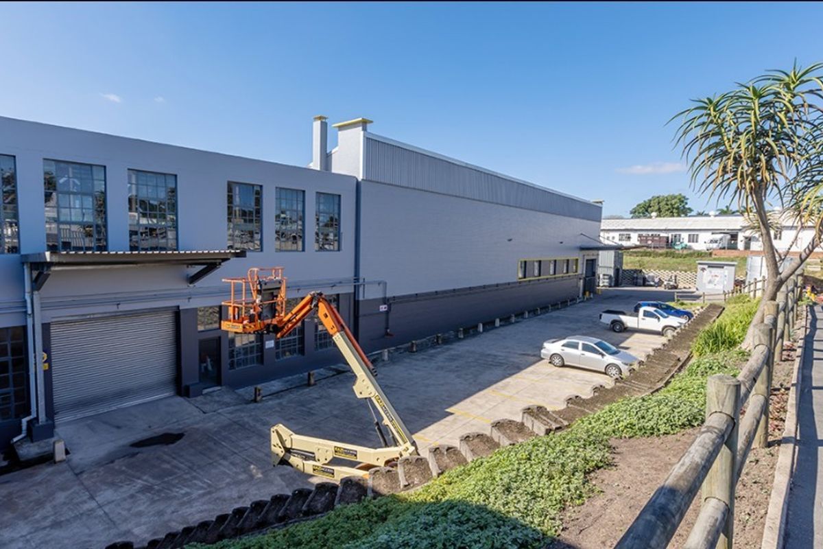 Rear exterior view of a commercial industrial building featuring a concrete yard, roller shutter access, and modern metal cladding.