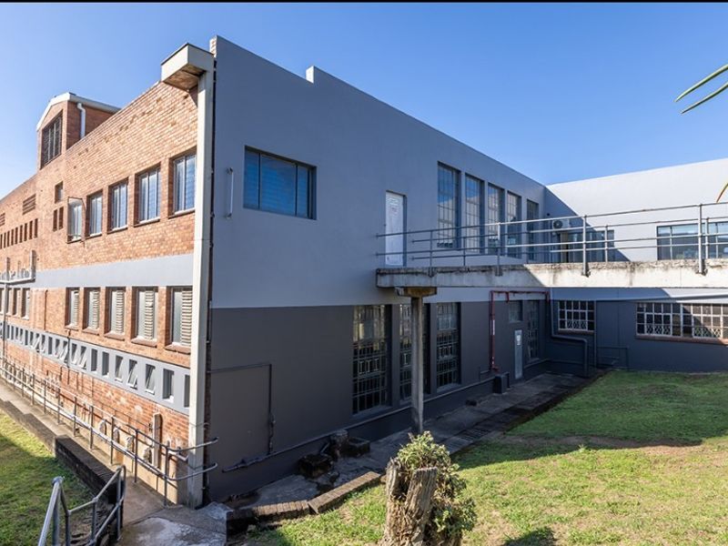 Rear exterior view of a multi-story commercial building featuring industrial brick and painted concrete facade with an elevated concrete walkway.