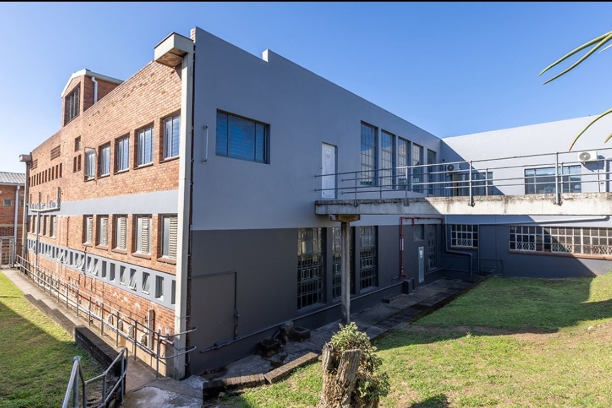 Rear exterior view of a multi-story commercial building featuring industrial brick and painted concrete facade with an elevated concrete walkway.