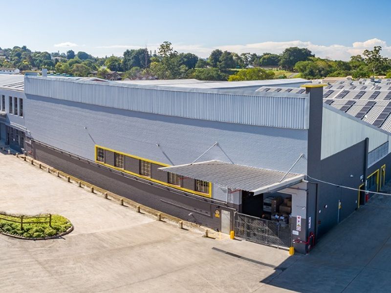 Aerial view of a commercial industrial facility featuring a large warehouse structure with solar panels, concrete yard space, and a dedicated loading bay area.