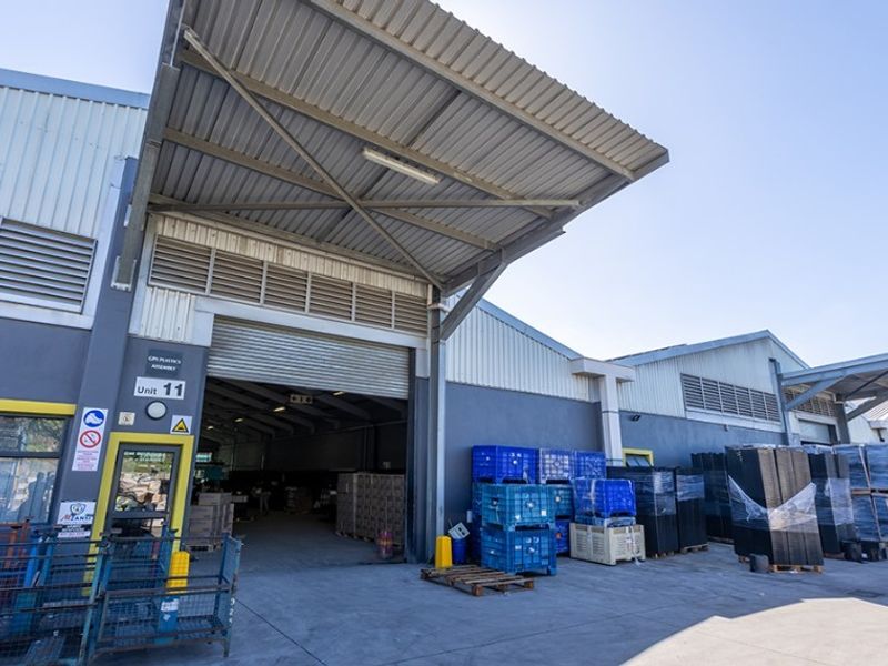 Commercial industrial unit featuring a large roller shutter door, steel canopy, and concrete loading area, suitable for warehouse or light manufacturing operations.