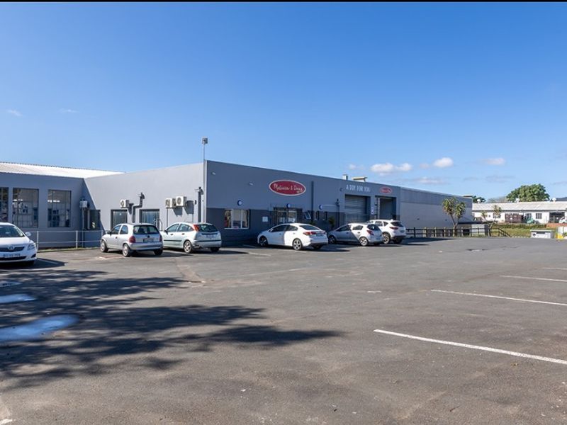 Commercial industrial property featuring a large asphalt parking area and a functional facade with roller shutter access points.