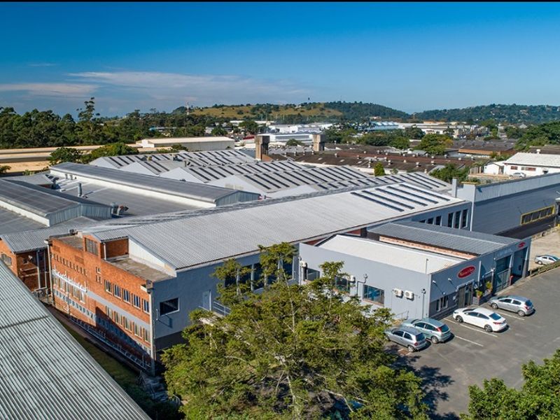 Aerial view of a large commercial industrial facility featuring extensive corrugated metal roofing, brick and painted masonry facades, and an adjacent asphalt parking area.