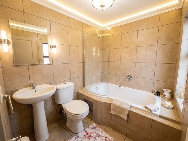 A well-maintained bathroom featuring a pedestal basin, toilet, and a built-in bathtub with a glass shower screen, finished with neutral wall and floor tiles.