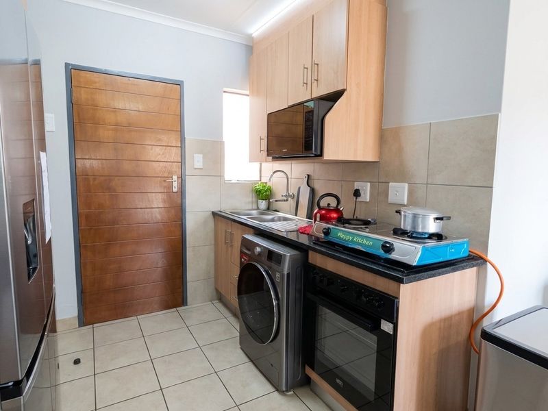 Compact kitchen featuring light wood cabinetry, granite countertops, tiled backsplash, and integrated appliances including an oven and microwave.
