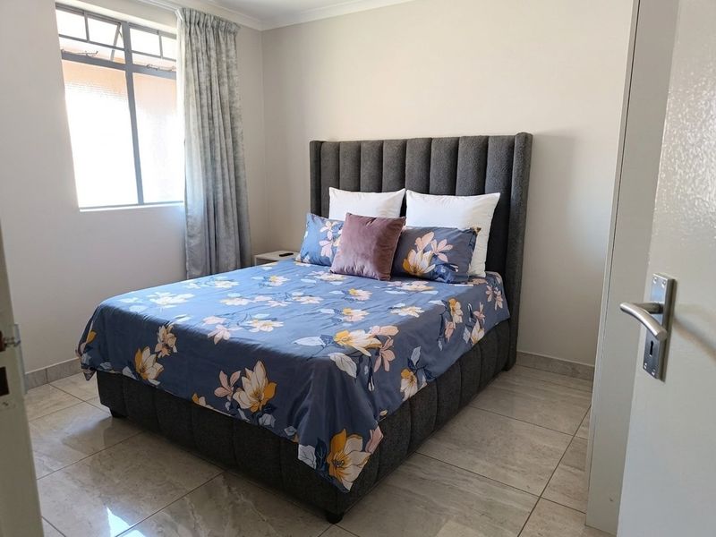 A well-maintained bedroom featuring neutral wall finishes, tiled flooring, and a large window that provides natural light.