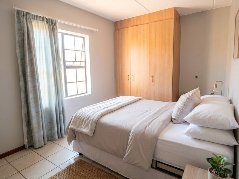 A well-lit bedroom featuring neutral walls, tiled flooring, and a functional built-in wooden wardrobe.