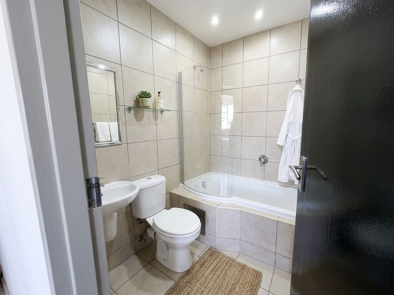 A well-maintained bathroom featuring a pedestal basin, toilet, and a bathtub with a glass shower screen, finished with neutral wall tiling.