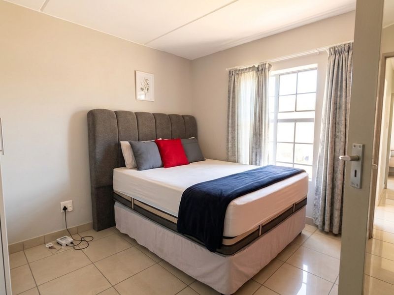A well-lit bedroom featuring neutral wall tones, tiled flooring, and a window with curtains, providing a clean and functional living space.