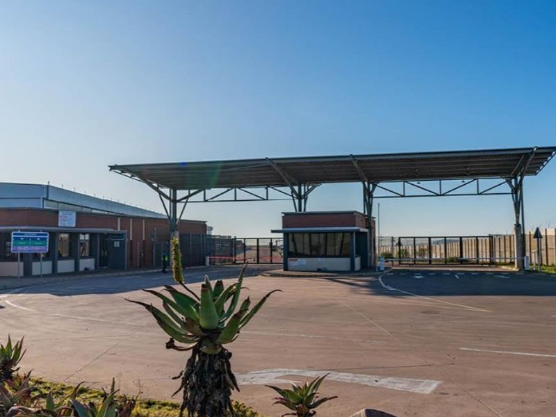 A view of the property entrance featuring a security gatehouse, large metal canopy, and paved driveway access.