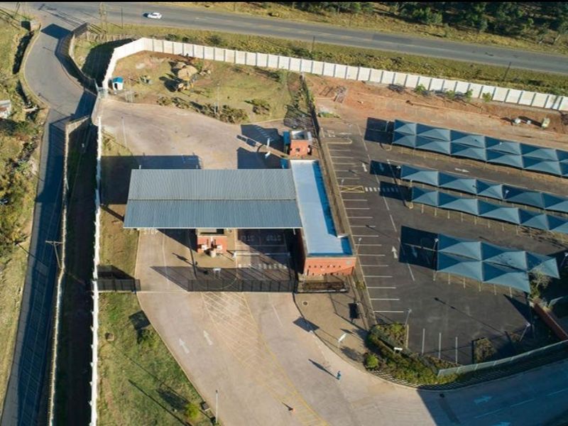 Aerial view of a secure agricultural property featuring a gated entrance, paved driveway, and extensive shaded parking facilities.