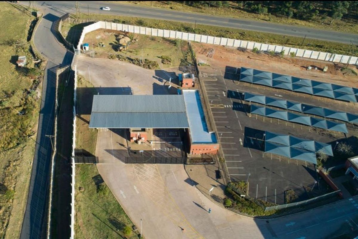 Aerial view of a secure agricultural property featuring a gated entrance, paved driveway, and extensive shaded parking facilities.