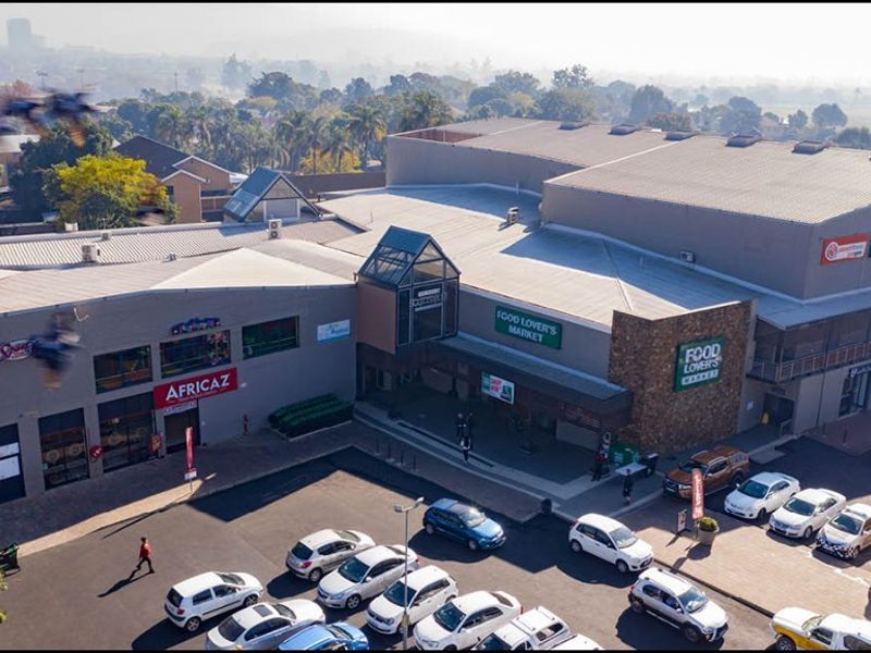 Aerial view of a retail shopping center featuring a large parking area, metal roofing, and prominent commercial storefronts.