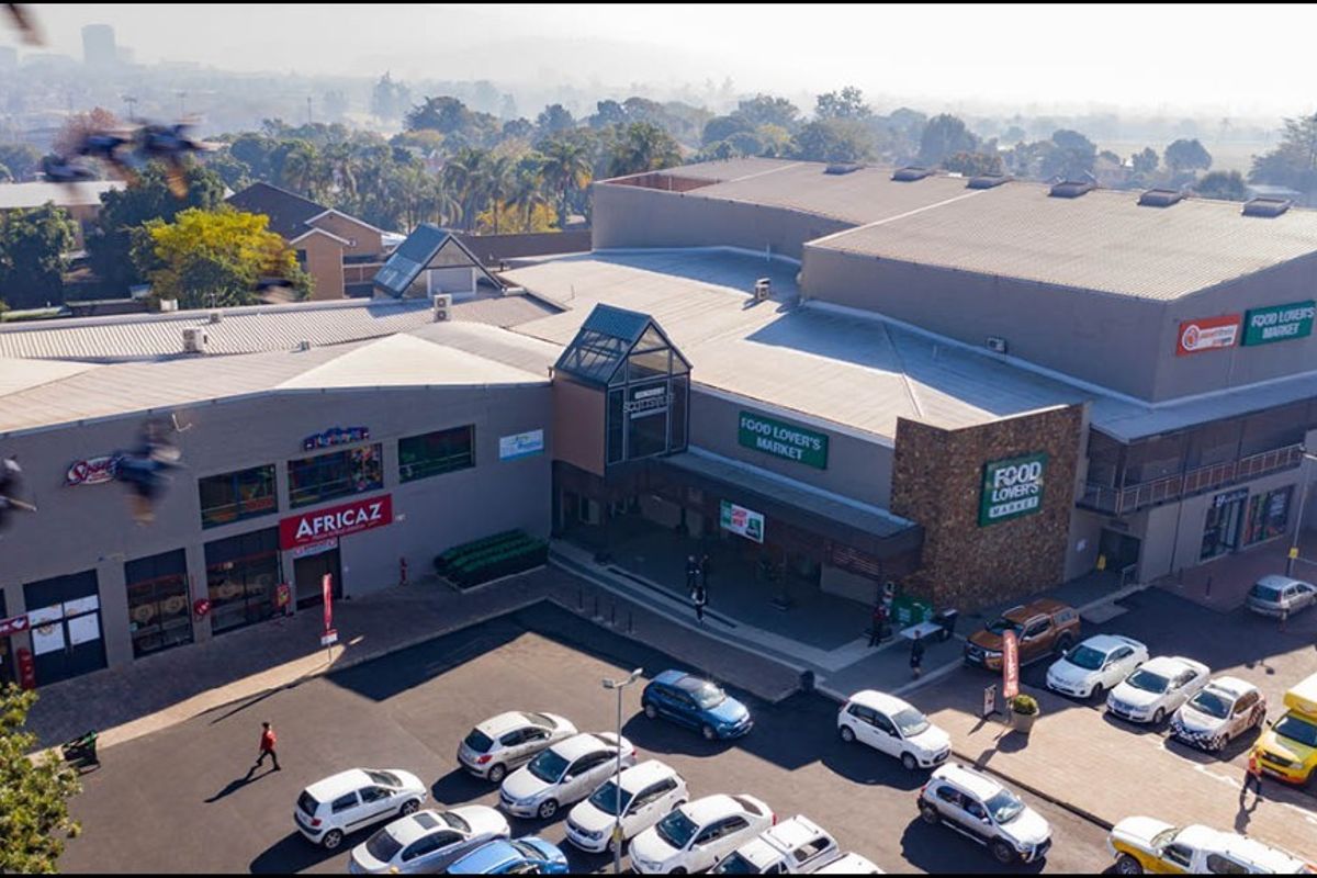 Aerial view of a retail shopping center featuring a large parking area, metal roofing, and prominent commercial storefronts.