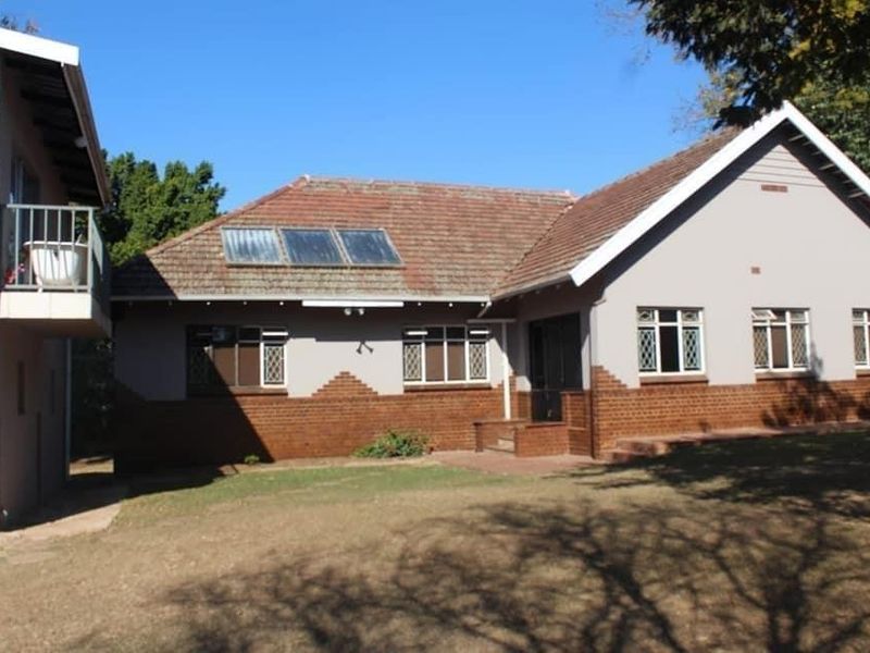 Rear view of a residential house featuring a tiled roof with solar panels, brick and plaster facade, and an upper-level balcony.