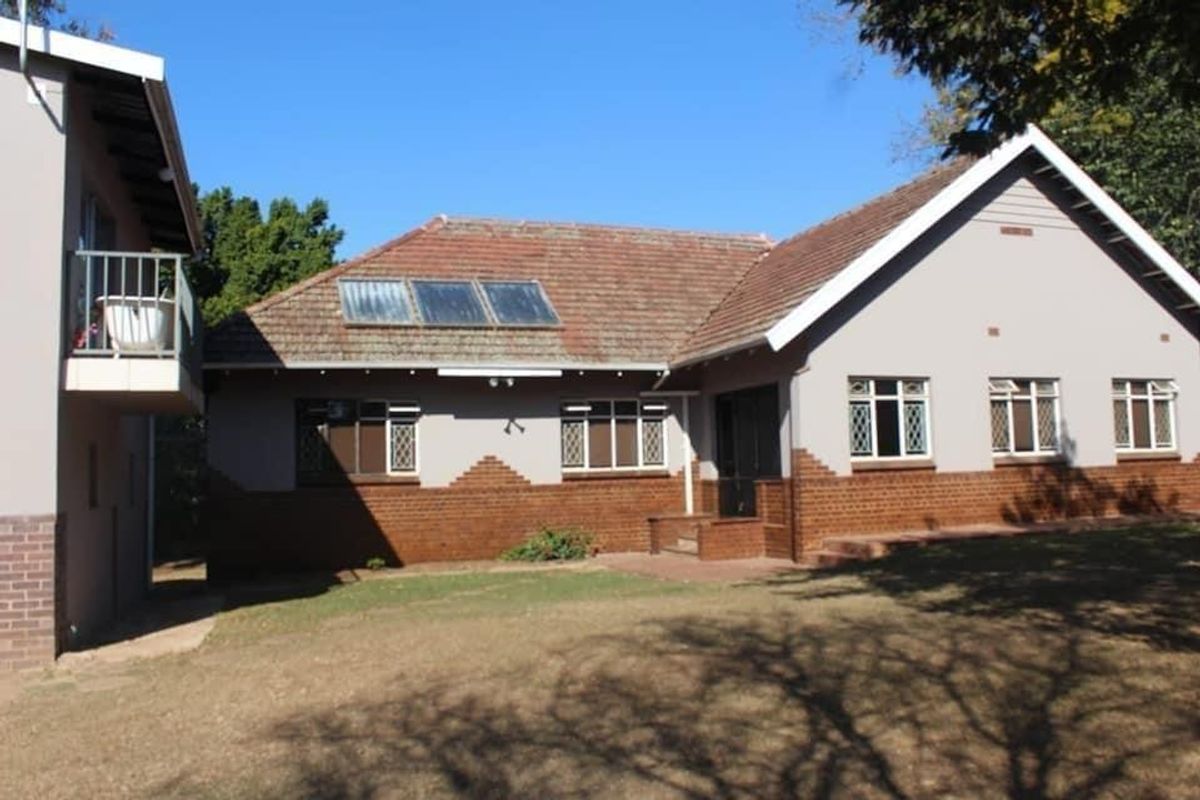 Rear view of a residential house featuring a tiled roof with solar panels, brick and plaster facade, and an upper-level balcony.