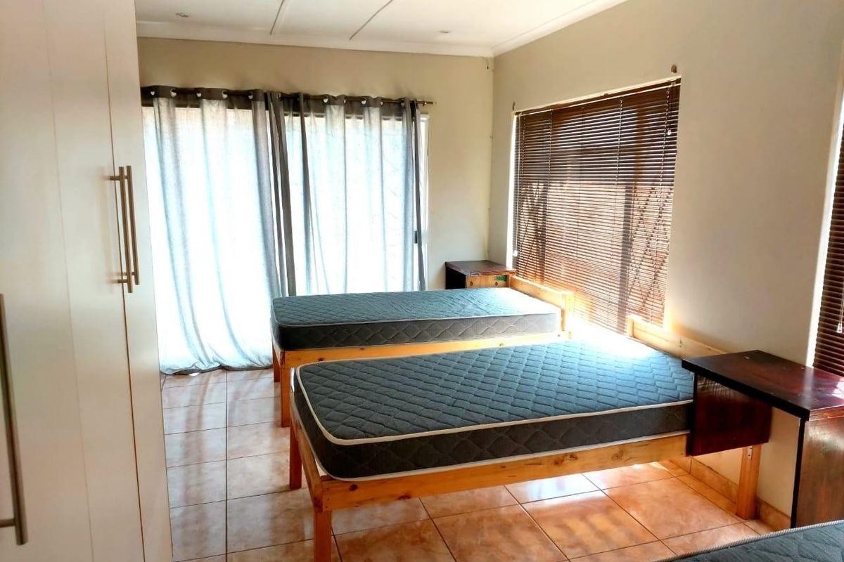 A functional bedroom featuring tiled flooring, built-in cupboards, and large windows with venetian blinds, providing ample natural light.