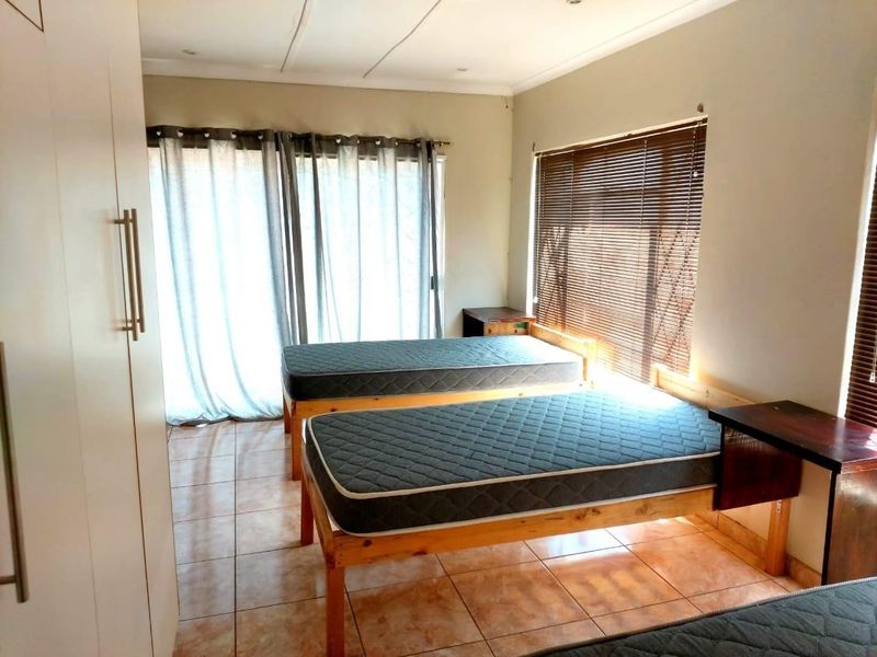 A functional bedroom featuring tiled flooring, built-in cupboards, and large windows with venetian blinds, providing ample natural light.