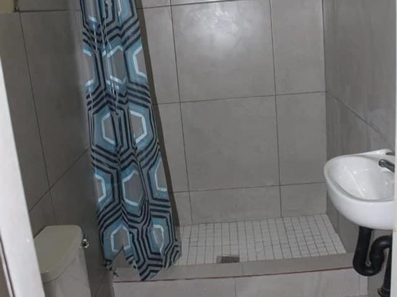 A compact bathroom featuring a walk-in shower with tiled walls, a wall-mounted basin, and a standard toilet.