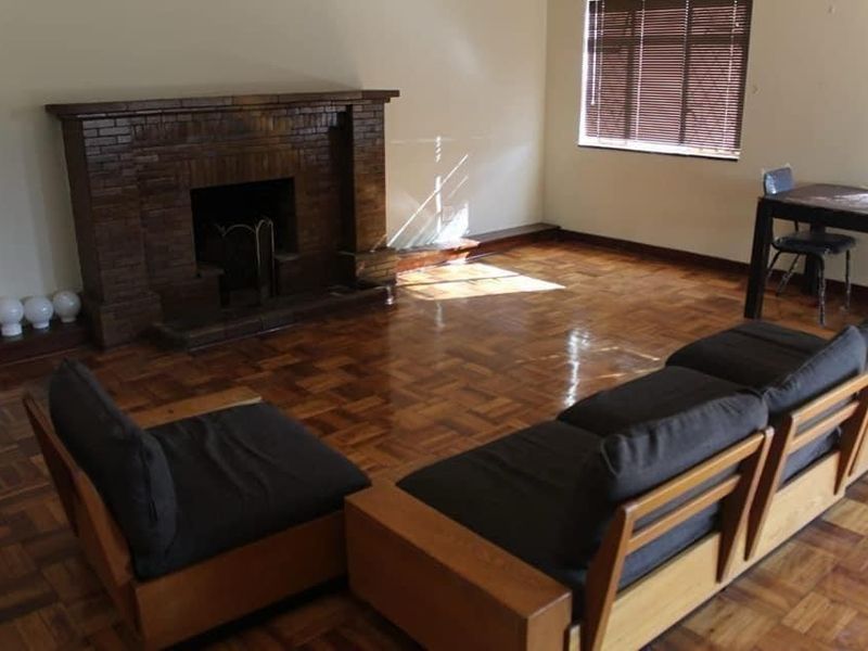 Spacious living room featuring classic parquet flooring and a prominent brick fireplace, offering a warm and traditional atmosphere.