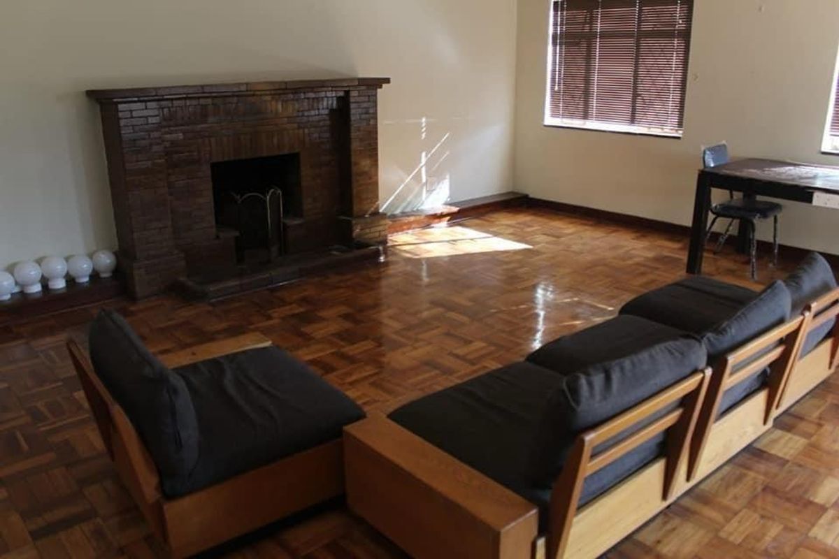 Spacious living room featuring classic parquet flooring and a prominent brick fireplace, offering a warm and traditional atmosphere.