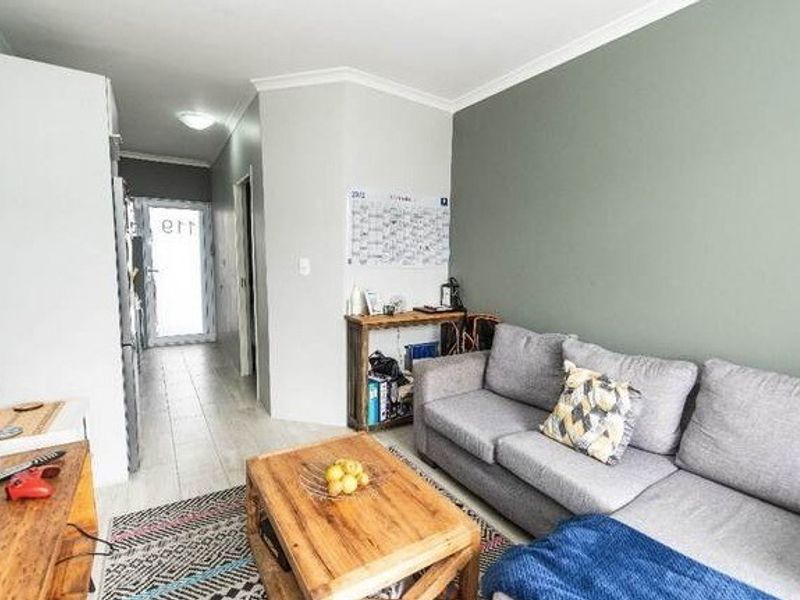 A living room featuring tiled flooring, coving, and a neutral color palette with an accent wall, leading to a hallway entrance.
