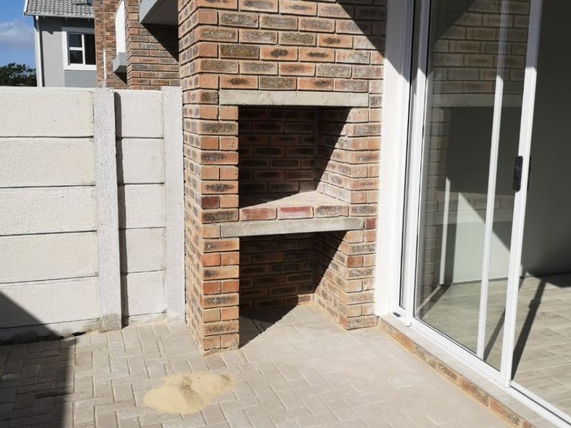 A private patio area featuring a built-in brick braai, paved flooring, and direct access to the interior through a sliding glass door.