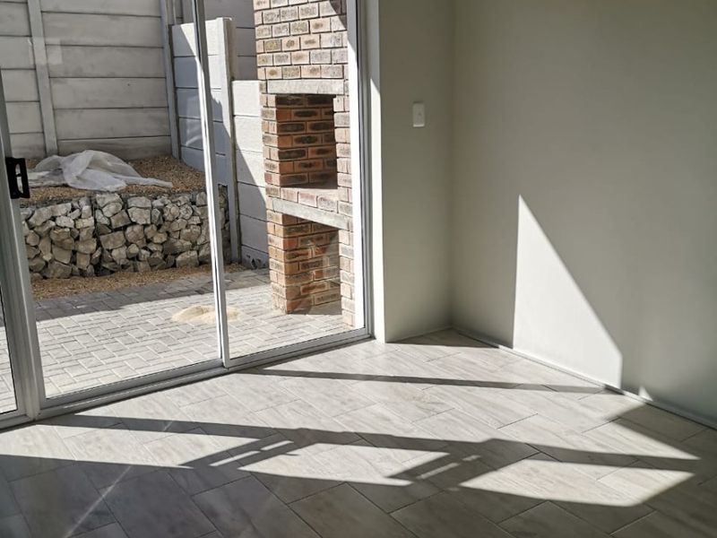 Bright, empty living area featuring modern tiled flooring and large sliding glass doors that open onto a private patio with a built-in brick braai.