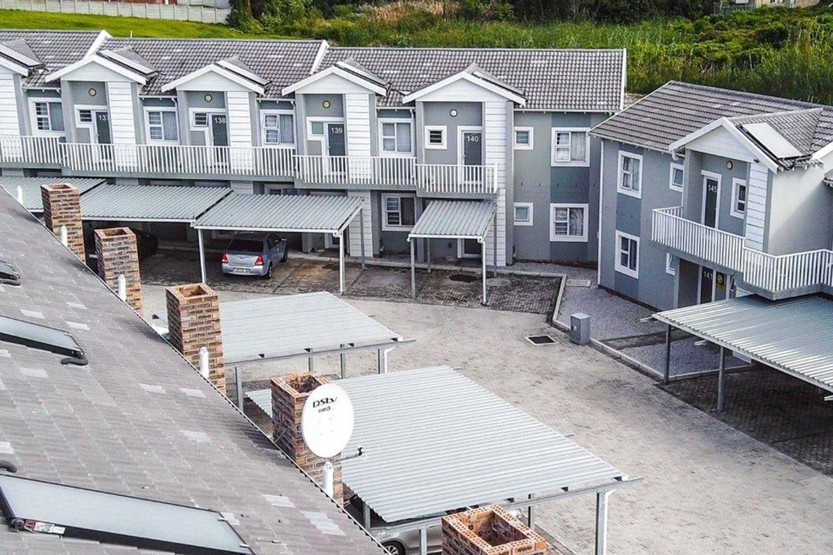 An aerial view of a modern apartment complex featuring multiple units with balconies, covered carports, and paved parking areas.