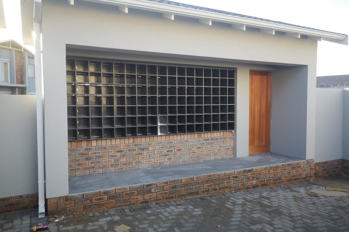 Rear exterior view of an apartment featuring a paved patio, brick base detailing, a timber door, and a built-in grid shelving unit.