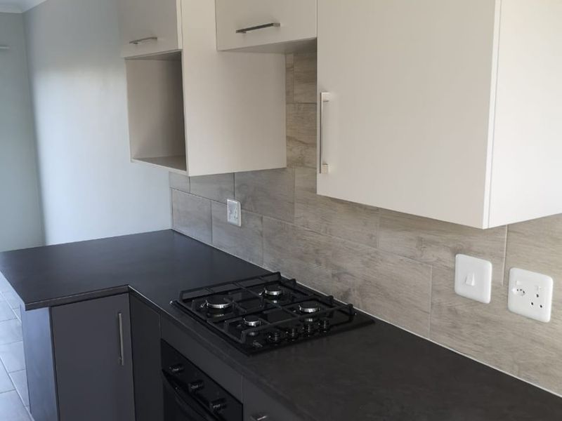 Modern kitchen featuring dark grey cabinetry, contrasting stone-look tile backsplash, built-in gas hob, oven, and sleek laminate countertops in a clean, contemporary space.