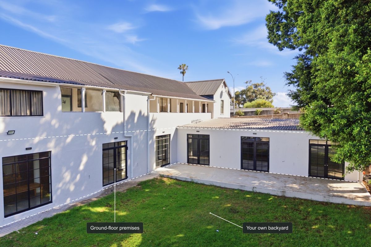 Rear view of the office building featuring a private lawn area, concrete patio, and multiple black-framed glass doors providing direct access to the ground-floor premises.