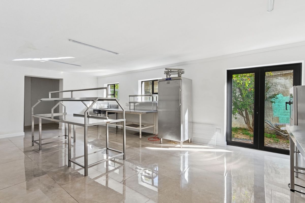 A clean, commercial-style kitchen space featuring stainless steel prep stations, a large refrigerator, polished tile flooring, and direct access to an outdoor area.